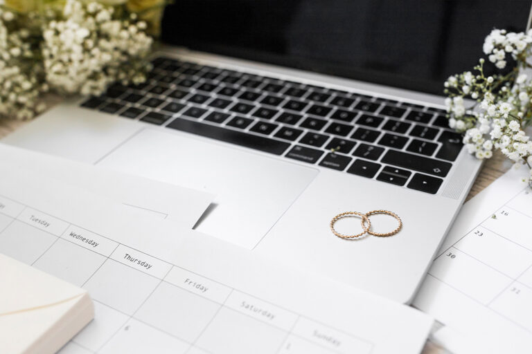 Un computer portatile Mac con due fedi poggiate sopra e un planner, ovvero gli elementi che raffigurano il wedding marketing